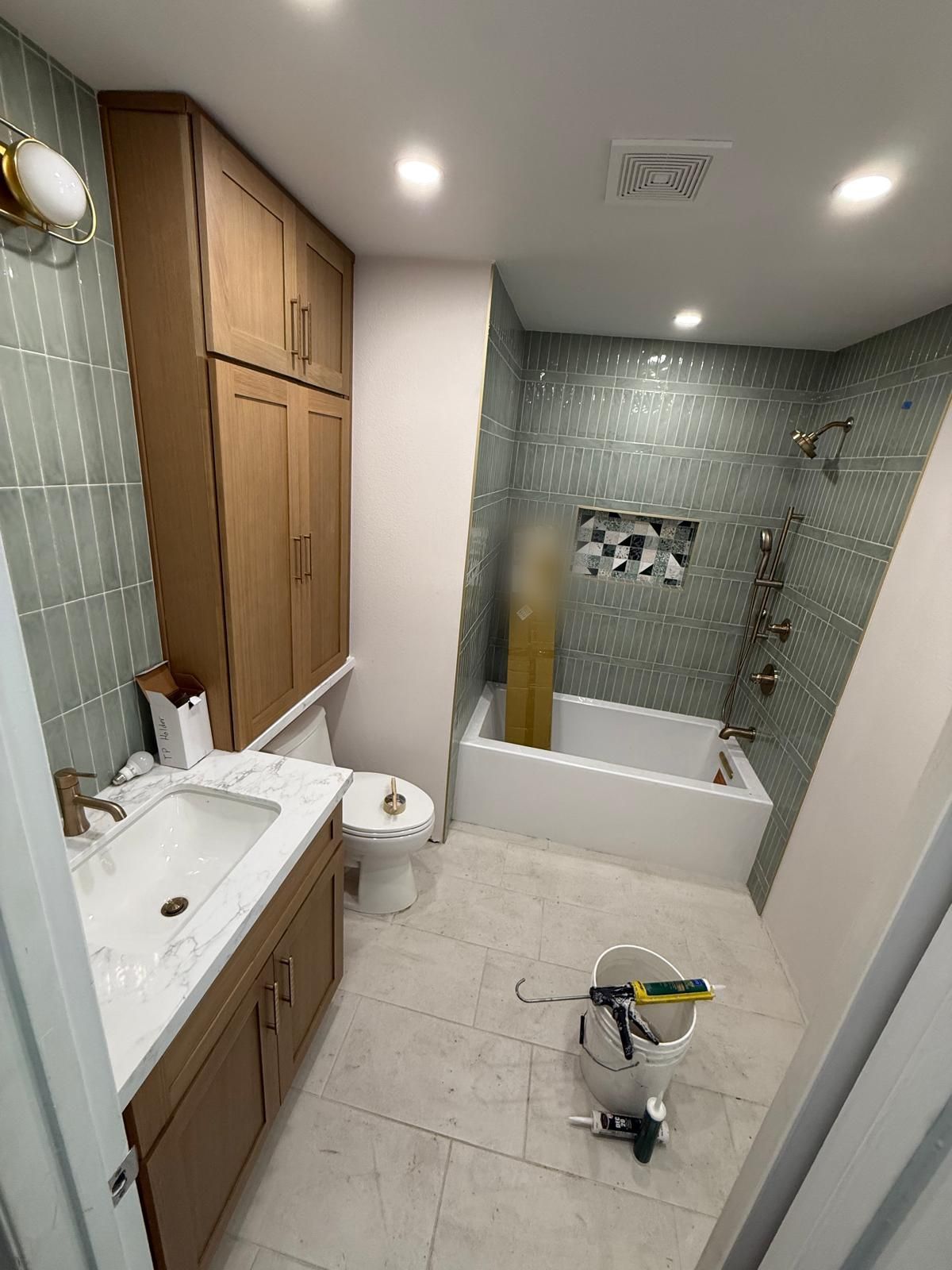 Remodeled bathroom with stacked sage green tile, a white oak vanity and linen tower, a terrazzo tile niche, and brushed brass fittings.