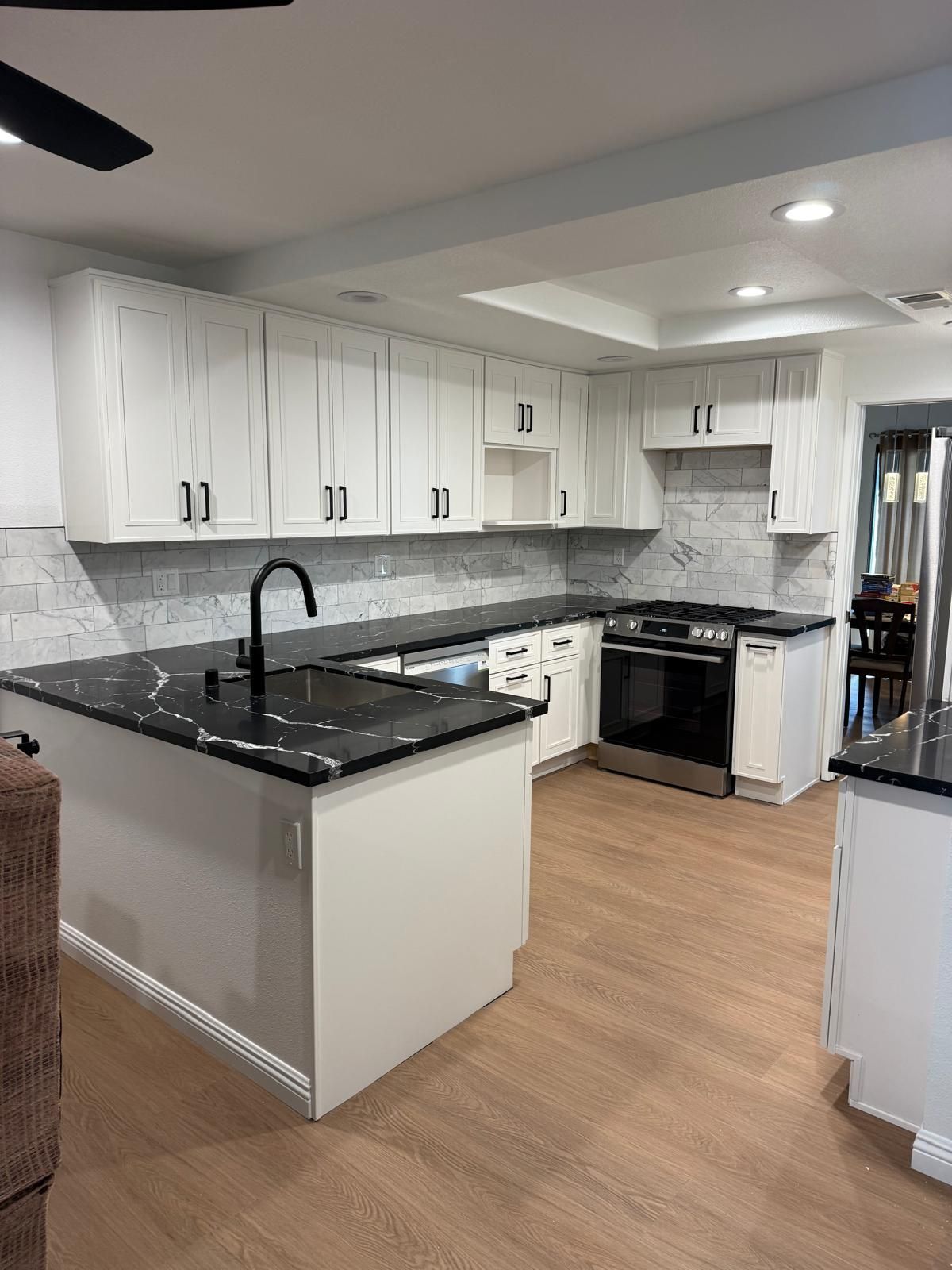 Finished kitchen with white shaker cabinets, black quartz peninsula counters, a marble subway backsplash, and a stainless gas range.