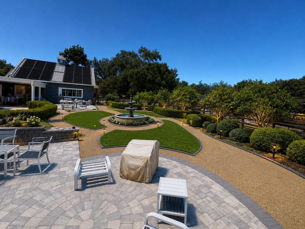The same yard finished with shaped lawn panels, gravel paths, a tiered stone fountain, low path lighting, clipped hedges, citrus trees, and the circular paver patio in the foreground.